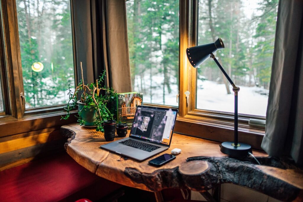 A well-organized, clutter-free workspace with a minimalist aesthetic. A softly lit desk displays a laptop, a planner, and a single potted plant, conveying a sense of focus and daily progress. The background features clean, neutral-toned walls, evoking a serene and calming atmosphere. Warm, natural lighting from a large window bathes the scene, creating a sense of warmth and productivity. The overall composition emphasizes simplicity, order, and efficiency, perfectly capturing the essence of "Breaking Down Tasks for Daily Progress." black and gray laptop computer beside black smartphone